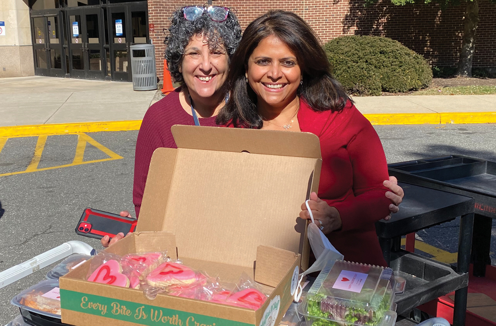 Two women standing near heart shaped cookies and other donated foods for employees